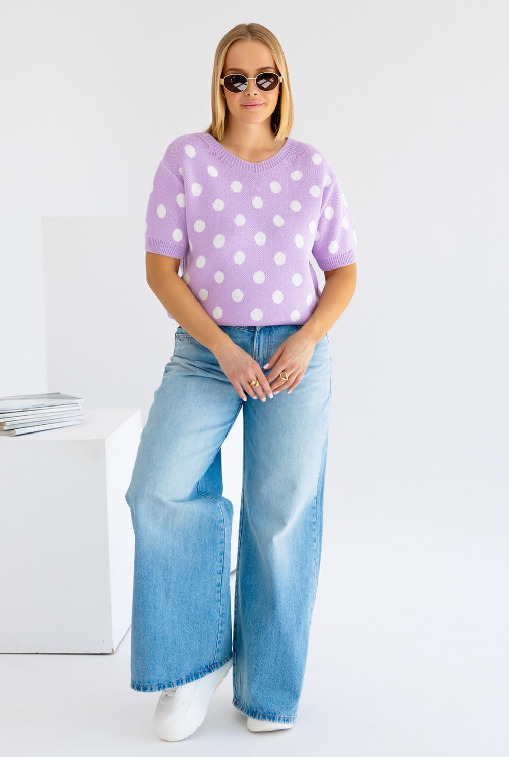 Damenpullover in Lila mit weißen Punkten, kombiniert mit weitem Jeans und Sonnenbrille.