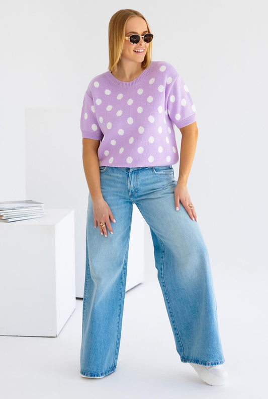 Lila Strickpullover Polka Dots mit weißen Punkten, lässig kombiniert mit weiten Jeans und Sonnenbrille.