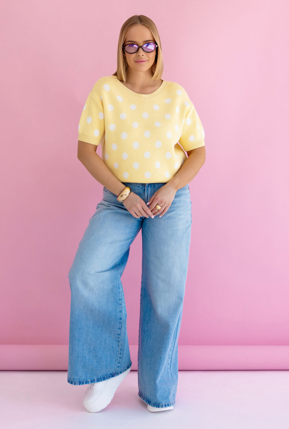 Gelber Polka Dots Strickpullover kurzarm, getragen von Modell mit blauen Jeans vor pinkem Hintergrund.