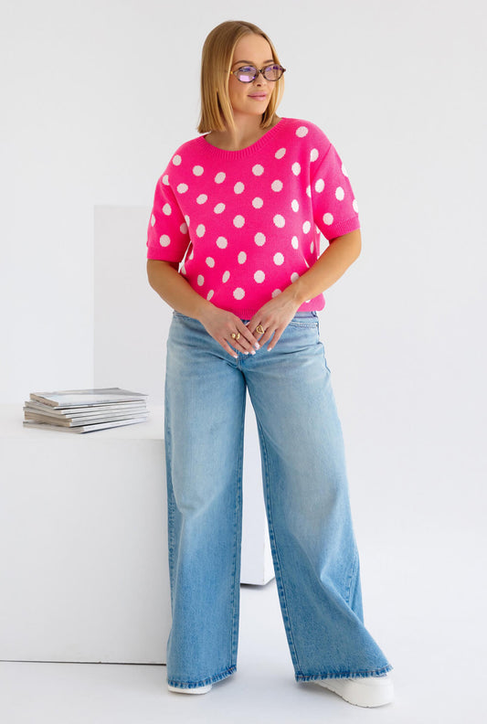 Strickpullover pink mit weißen Punkten, kombiniert mit lässigen Jeans und Sonnenbrille. Modischer Look.