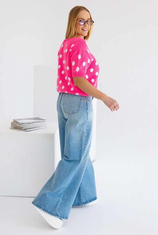 Frau trägt einen Polka Dots Strickpullover kurzarm in Pink mit weißen Punkten, kombiniert mit blauen Jeans.