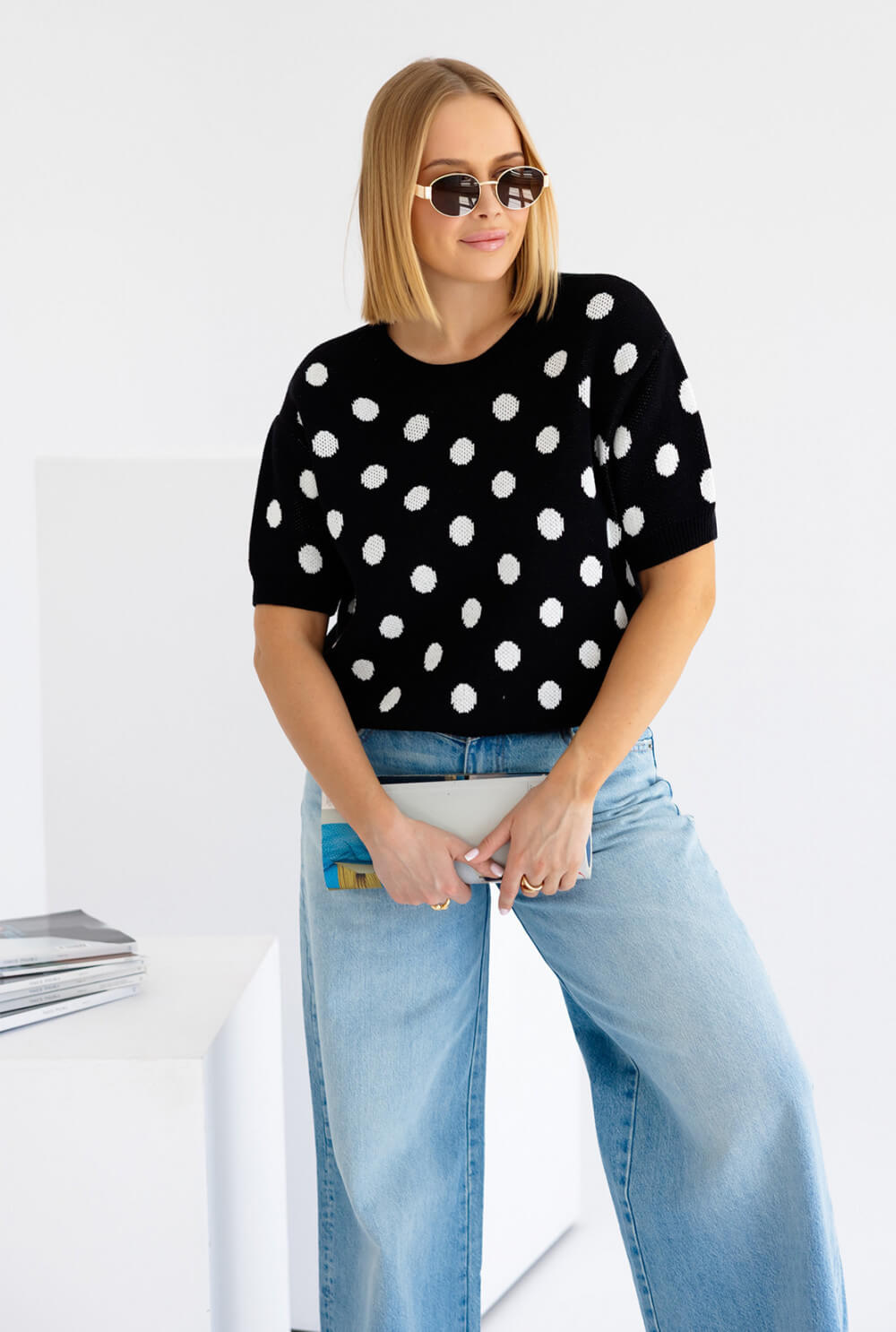 Polka Dots Strickpullover in Schwarz mit Weiß, kurzarm, kombiniert mit Jeans und Sonnenbrille.