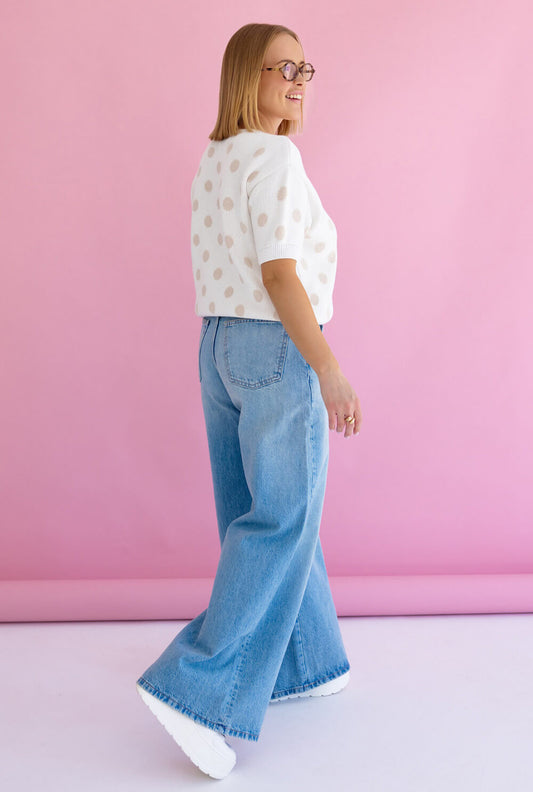 Weisser Strickpullover Polka Dots, stylisch kombiniert mit lässigen Jeans und weißen Sneakers.